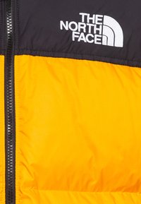 Puffa bunda s černou horní částí a živě oranžovou dolní částí. Obsahuje zipové zapínání a bílé vyšívané logo.