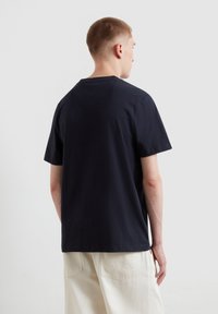 T-shirt in cotone blu navy con maniche corte, scollo rotondo semplice e vestibilità rilassata. Texture liscia e design minimalista.