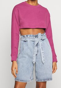 Korthälst lila ribbad sweatshirt med lång ärm och rund halsringning, tillsammans med högmidjade ljusblå jeansshorts med ett tygbälte.