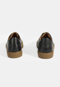 Baskets noires avec un dessus en cuir texturé, semelles en caoutchouc beige et un design sans lacets avec un dos bas.