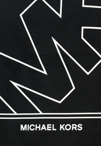 Μαύρο ύφασμα με τολμηρές λευκές γεωμετρικές γραμμές και κείμενο. Το σχέδιο περιλαμβάνει το όνομα "MICHAEL KORS" σε εμφανή, μοντέρνα γραμματοσειρά.