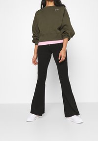 Sudadera oversize verde oliva con un dobladillo rosa, combinada con pantalones de canalé negros de pata de elefante y zapatillas blancas. Diseño simple y casual.