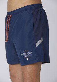 Costumi da bagno blu navy con vita elastica, lacci arancioni, dettagli laterali argentati e logo ricamato sulla gamba inferiore.