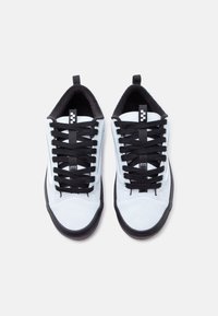 Λευκά αθλητικά παπούτσια με μαύρες σόλες, μαύρα κορδόνια και μαύρη εσωτερική επένδυση, σε θέα από πάνω πάνω σε απλό φωτεινό φόντο.