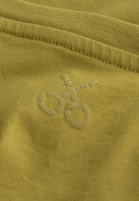 Tessuto in cotone verde con una morbida texture, caratterizzato da un discreto logo a forma di forbici ricamato in una tonalità leggermente più chiara.