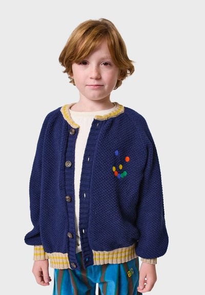 Mornarica pletena jakna s žutim detaljima, zakopčana sprijeda, s raznobojnim vezom na lijevoj strani. Ima rebraste manšete i donji rub.