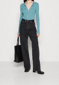 Maglione a maniche lunghe a coste in teal con collo a camicia e chiusura con bottoni, abbinato a jeans neri a gamba larga con vita alta e una borsa tote nera.