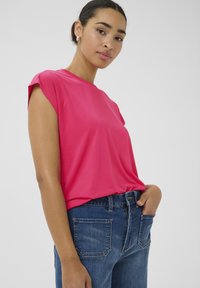 Fuchsia Kurzarmoberteil aus glattem Stoff, kombiniert mit dunkelblauen Jeans mit hoher Taille und klassischem Fünf-Taschen-Design.