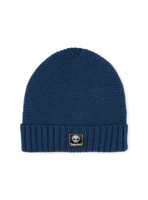 Bonnet en tricot de couleur bleu foncé avec un revers côtelé. Présente une petite étiquette carrée noire avec un logo blanc. Texture douce et forme arrondie.