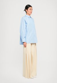 Blue and white striped oversized shirt with long puff sleeves and a button collar, paired with wide beige pleated trousers.