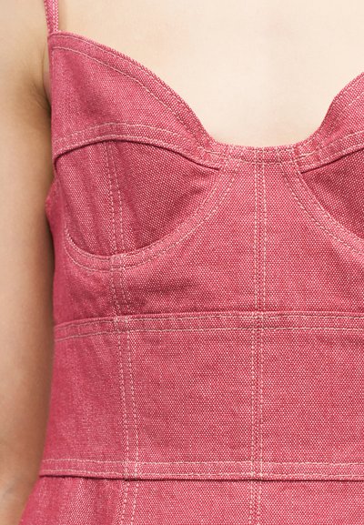 Gros plan sur une personne portant un haut rose texturé sans manches avec des coutures visibles et un décolleté en forme de cœur.