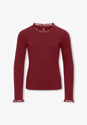 Langermet, ribbestrikket topp i dyp rød med rund hals med gjennomsiktig volangkant og rysjekanter. Mykt teksturert stoff.