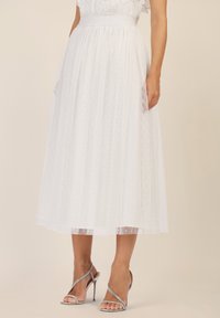 Falda midi blanca de tela ligera y texturizada con un patrón de lunares. Presenta una cintura alta y bolsillos laterales. Combínala con tacones plateados.
