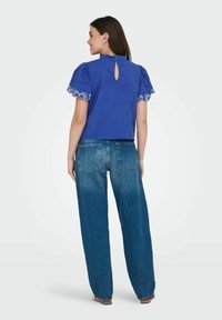 Top in cotone blu con maniche a sbuffo e orlo ricamato bianco, dotato di apertura a chiave sul retro. Abbinato a jeans in denim blu a vita alta.