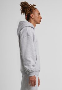 Pilkas džemperis su minkšta medžiaga, turintis erdvų gobtuvą, raukšlėtus rankogalius ir kengūros kišenę; paprastas, laisvas siluetas su minimaliais akcentais.