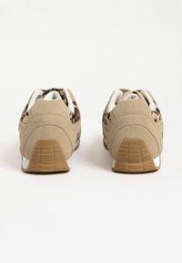 Beżowe sneakersy o zamszowym wykończeniu, z wzorzystymi akcentami na bokach, białymi sznurówkami i gumową podeszwą. Widok z tyłu ukazuje teksturowany obcas i wzór bieżnika.