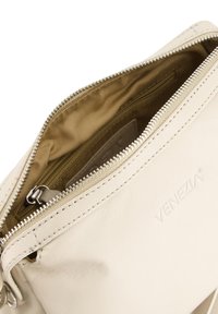 Beige Lederhandtasche mit Reißverschluss, ausgestattet mit einem braunen Stoffinnenfutter und geprägtem Logo. Glatte Textur und saubere Nähte.