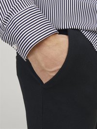 Blau-weiß gestreifte Hemdbluse mit Knopfmanschette, kombiniert mit schwarzen Stoffhosen mit Seitentasche. Glatte Textur, taillierte Passform.