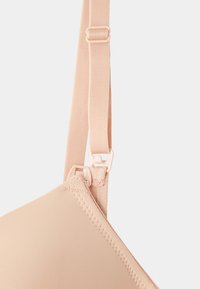 Light beige bra with smooth fabric, adjustable strap, and hook closure. Notable for its seamless design and soft texture.