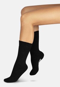 Schwarze Baumwollsocken mit einem gerippten Design, ausgestattet mit einem dicken Bündchen und einem weißen Markenlogo an der Seite. Weiche Textur und knöchellänge.