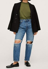 Czarna dwurzędowa marynarka na oliwkowym swetrze z okrągłym dekoltem, połączona z jasnoniebieskimi dżinsami z przetarciami i czarnymi lordami. Szczegóły casualowego stroju.