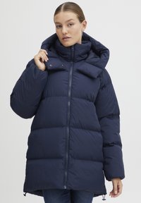 Navy blue padded coat with a high collar and oversized hood, featuring a front zipper and snap buttons, smooth texture, and a relaxed fit.