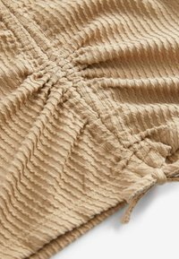 Textureret beige stof med bølgede striber, der har sammensamlede sektioner og en bundet detalje. Blødt og let materiale, ideelt til tøj.