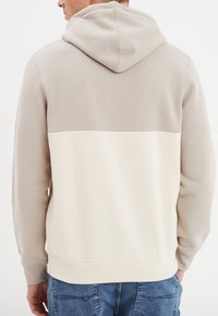 Sudadera con capucha en beige y crema, con un diseño de bloques de color y una textura suave. Cuenta con una capucha con cordón y un dobladillo acanalado.