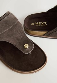 Sandales en daim marron avec un bouton doré, semelle en liège et marquage "NEXT Forever Comfort" visible à l'intérieur.