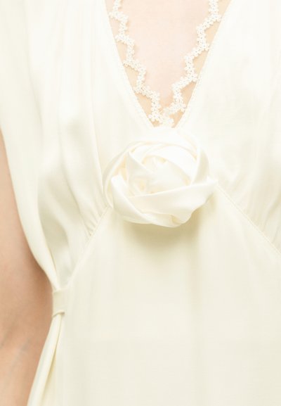 Robe crème avec un décolleté en V profond orné d'une bordure en dentelle et d'une décoration en forme de rose en tissu au centre du corsage avant.