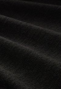 Schwarzer Stoff mit einer strukturierten Oberfläche, der weiche, feine Fasern und subtile Farbschattierungen über die Falten des Materials aufweist.