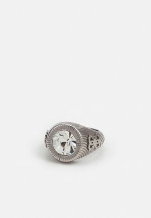 Silberner Ring mit großem klarem rundem Edelstein und dekorativen eingravierten Mustern am Band vor einfachem weißem Hintergrund.