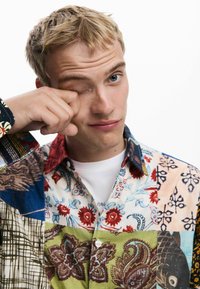 Camisa de patchwork multicolor con patrones florales, de paisley y geométricos, con cuello extendido y botonadura frontal.