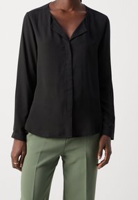 Blusa nera a maniche lunghe realizzata in tessuto morbido, con una vestibilità comoda, caratterizzata da un collo rotondo e una chiusura a bottoni discreta.