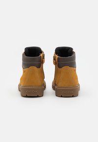 Botines de ante marrón con un cuello acolchado gris, que presentan una cremallera trasera y suela de goma texturizada, marcada con el logo de GEOX.