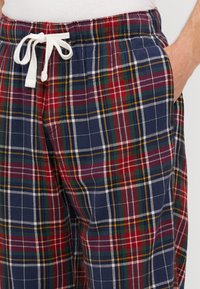 Pantalons lounge à carreaux avec une base bleu marine et des lignes rouges, vertes et jaunes. Taille élastique avec un cordon de serrage blanc et poches latérales.