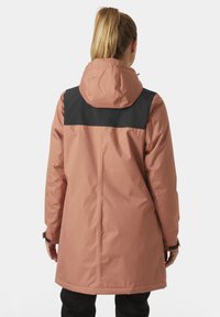 Chaqueta impermeable rosa con un panel trasero negro, que cuenta con capucha, mangas largas y puños ajustables. Textura suave y diseño de longitud media.