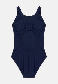 Μονόχρωμο μαγιό σε σκούρο μπλε ναυτικού χρώματος με φαρδιές τιράντες και μεγάλο οβάλ άνοιγμα στην πλάτη, τοποθετημένο επίπεδα πάνω σε λευκό φόντο.