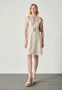 Beige belted kjole med korte ermer, knappefeste foran og ribbet tekstur. Kombinert med brune espadriller med kilehæl og en lys brun veske.