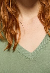 Pull en maille col en V vert clair. Présente un col côtelé et une texture subtile. Porté près de la clavicule.
