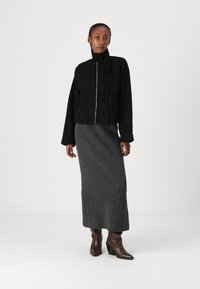 Black zip-up jacket with a high collar, paired with a ribbed gray maxi skirt and brown heeled ankle boots on a neutral background.
