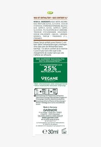 Genomskinlig plastetikett med grön och vit text på en transparent bakgrund, som beskriver ingredienser och information om återvinningsbar glas.