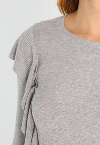 Maglione grigio lavorato a maglia con scollo a barca e tessuto strutturato, arricchito da dettagli a volant sulle spalle per un tocco più elegante.
