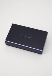Tumed sinine ristkülikukujuline karp, millel on valge "TOMMY HILFIGER" logo, all ääres on punased ja sinised triibud.