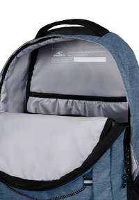 Interno di uno zaino di stoffa blu con fodera grigia, dotato di un ampio scomparto principale, tasca con zip e dettagli riflettenti.