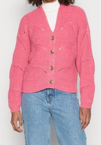 Rosa stickad kofta med V-ringning, med strukturerade mönster och fyra bruna knappar fram. Ribbad ärm och nederkant.