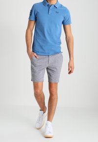 Světle modrá polo tričko s krátkým rukávem a límečkem, kombinované se šedými texturovanými šortkami. Bílé tenisky doplňují celý outfit.