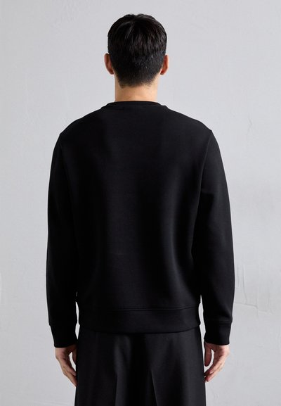 Black sweatshirt with long sleeves, round neckline, and ribbed cuffs and hem. Smooth texture, simple design, worn over black pants.