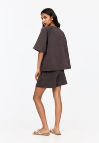 Bruine katoenen oversized t-shirt met korte mouwen, gecombineerd met bijpassende shorts. Platte sandalen met een decoratieve band. Eenvoudige, comfortabele pasvorm.