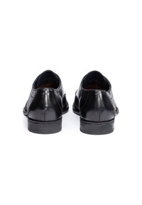 Chaussures en cuir noir avec une finition lisse, bout arrondi, petit talon et coutures discrètes. Ouvertures latérales pour un enfilage facile.